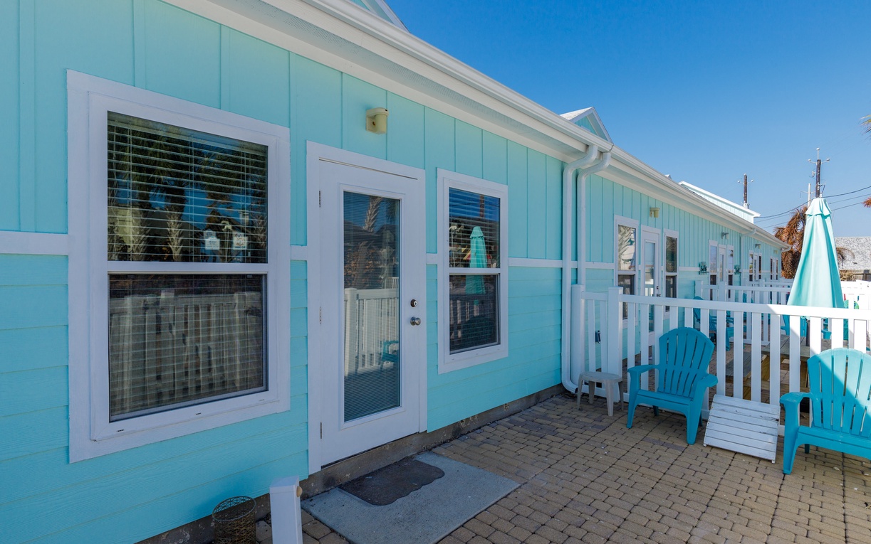 Charming turquoise beach cottage exterior with white trim and private patio featuring blue Adirondack chairs for relaxing coastal moments.
