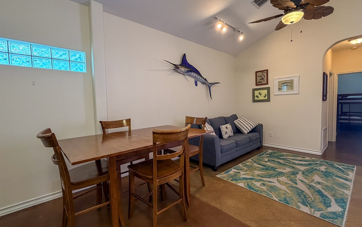 Gather around the warm wood dining table or relax on your cozy sofa in this bright, coastal-themed living space.