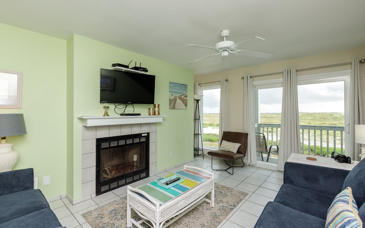 Relax in your coastal living room with fireplace, TV, and balcony doors opening to scenic views—perfect for unwinding after beach days.