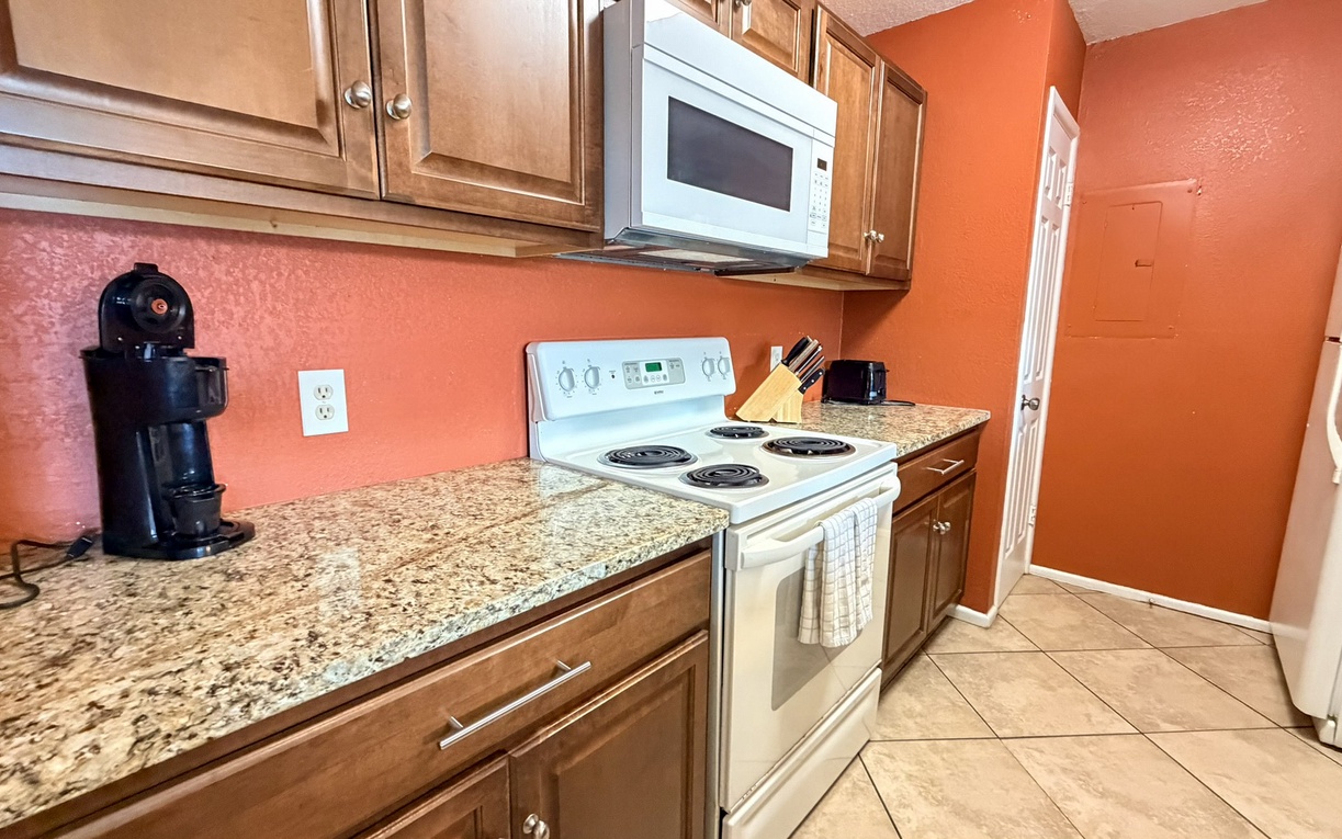 Your fully equipped kitchen features granite counters, modern appliances, and warm orange walls that create a cheerful space for preparing meals.