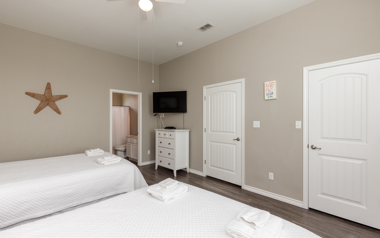 Unwind in your peaceful twin bedroom featuring comfortable beds, coastal decor, and modern amenities including TV and ensuite bathroom access.