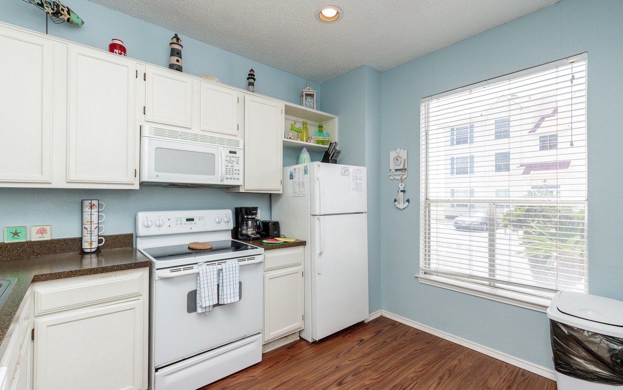 Your fully equipped kitchen features white appliances, ample storage, and peaceful views through large windows—perfect for preparing your favorite meals.