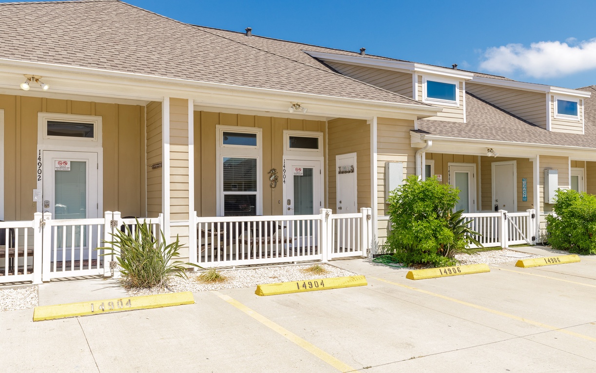 Multiple beige vacation rental units with covered porches and numbered parking spaces create a welcoming coastal community setting.