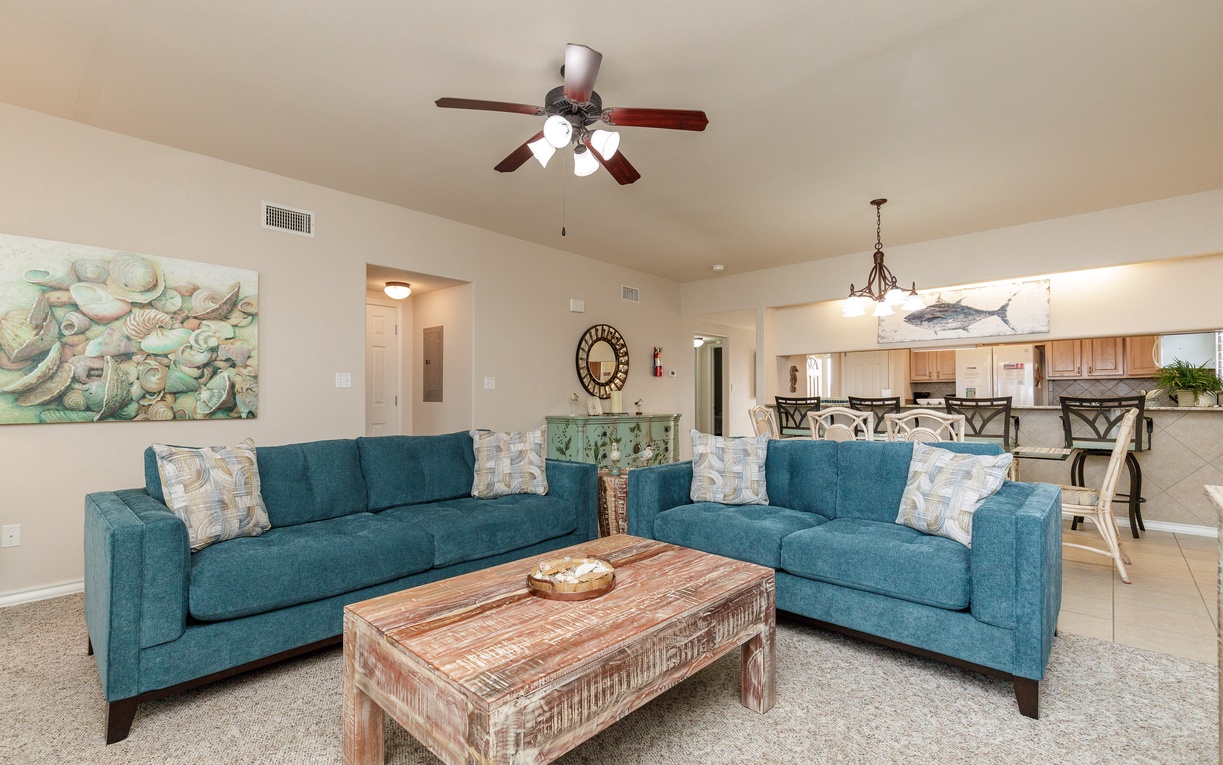 Sink into plush teal sofas and feel the ocean breeze from your ceiling fan in this coastal-inspired living space.