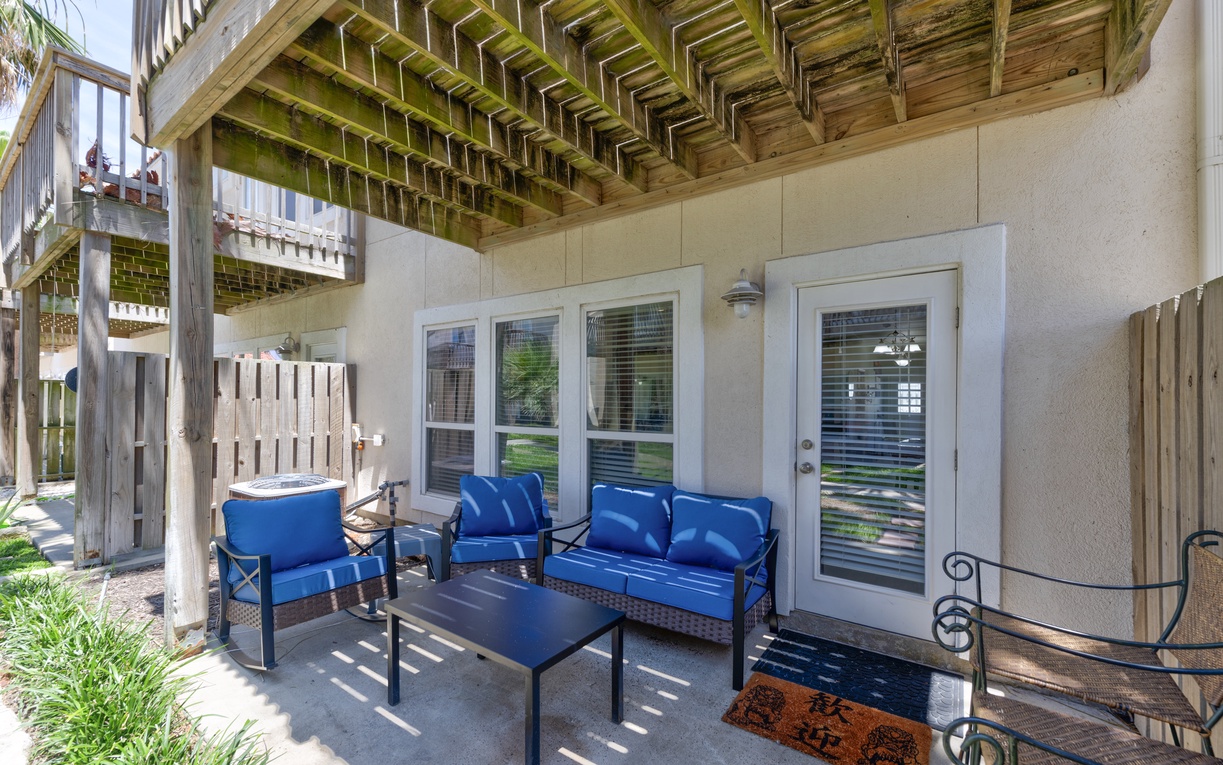 Step onto your private covered patio, where blue cushioned seating invites you to relax beneath charming wooden beams and enjoy the coastal breeze in peaceful comfort.