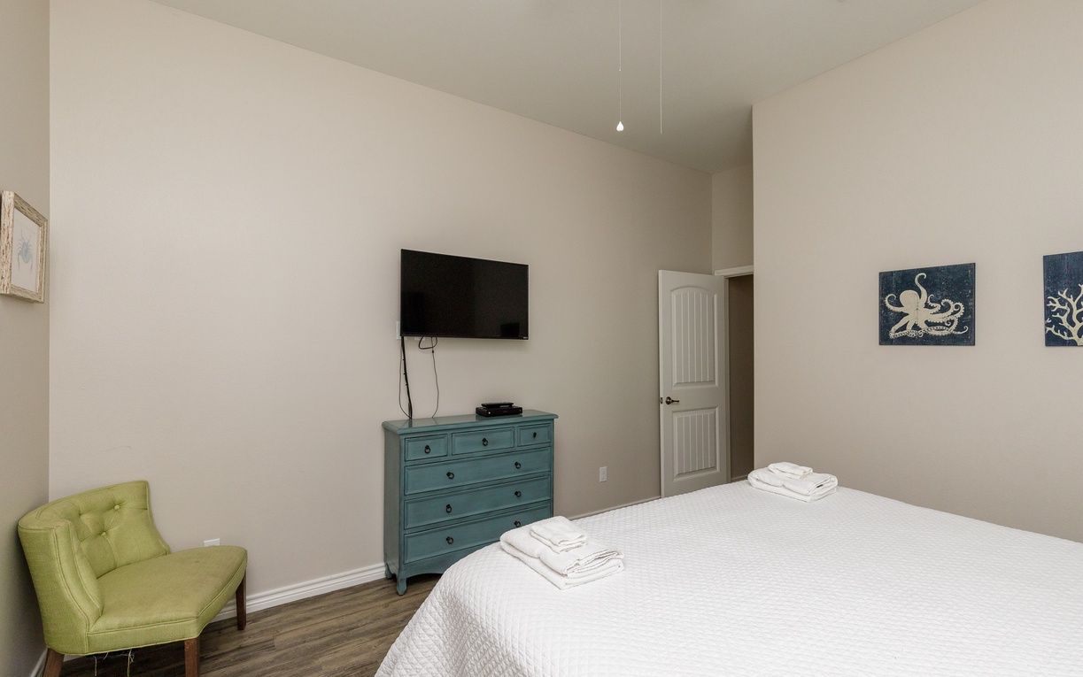 Relax in your serene bedroom featuring a plush queen bed, wall-mounted TV, and coastal-inspired decor that creates the perfect retreat.