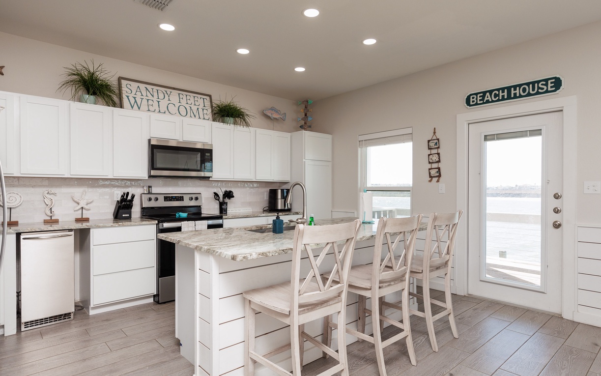 Your bright, coastal-themed kitchen awaits with a granite island for morning coffee and beach views through glass doors.