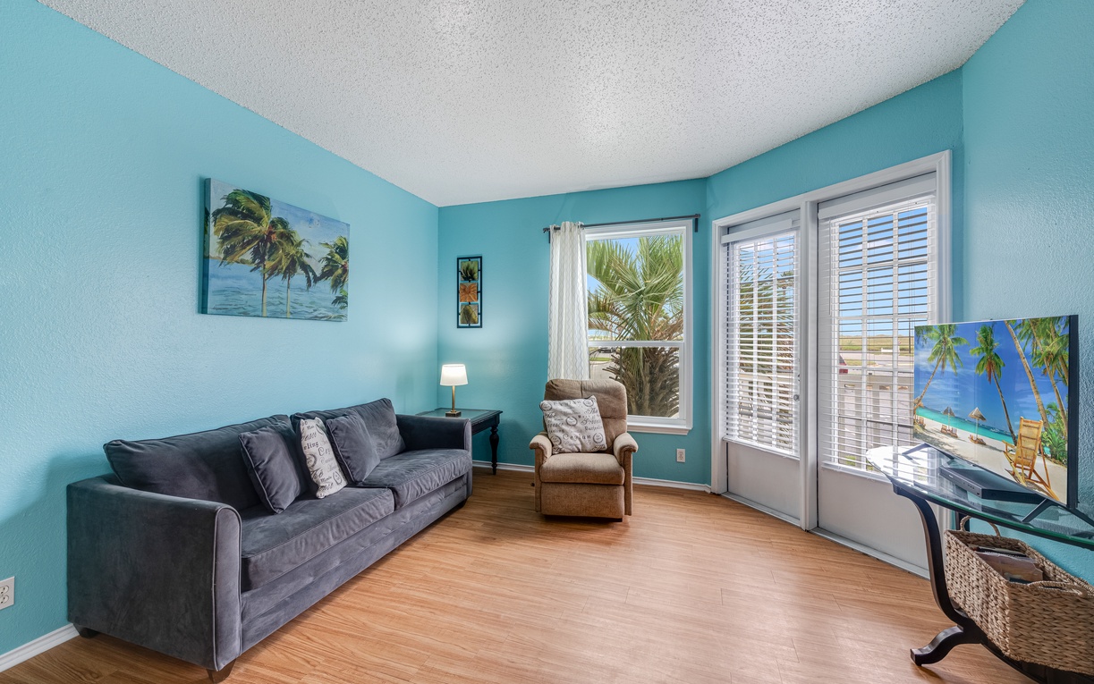 Relax in your bright coastal living room with tropical artwork, comfy seating, and serene turquoise walls that mirror ocean vibes.