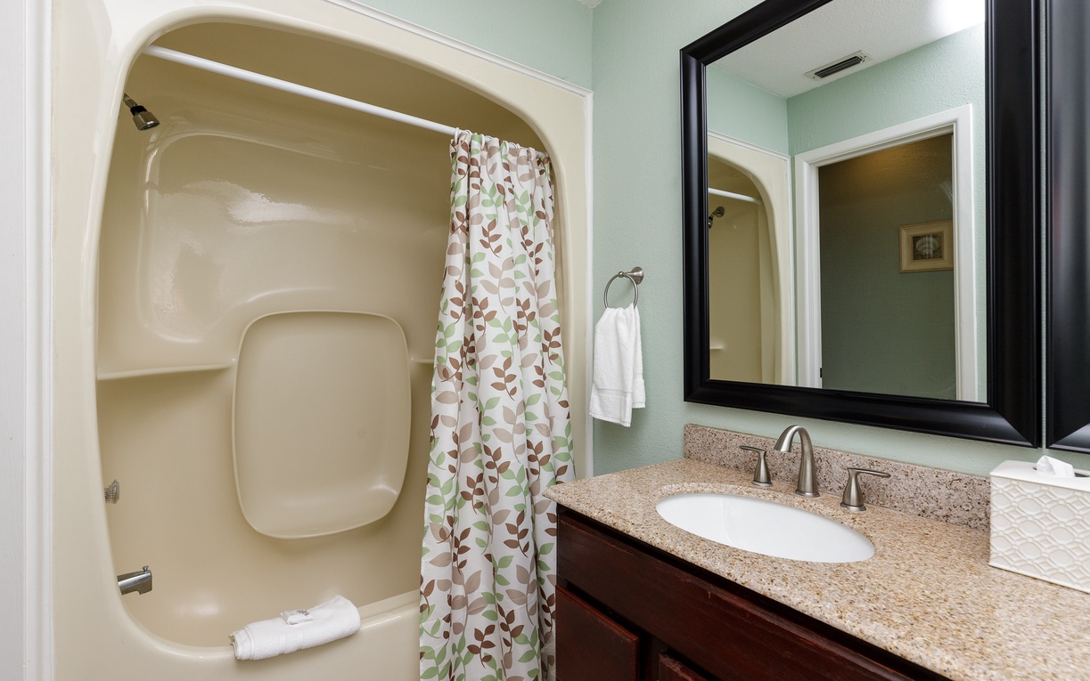 Step into your refreshing bathroom featuring a spacious tub-shower combo with cheerful botanical curtain and granite vanity.