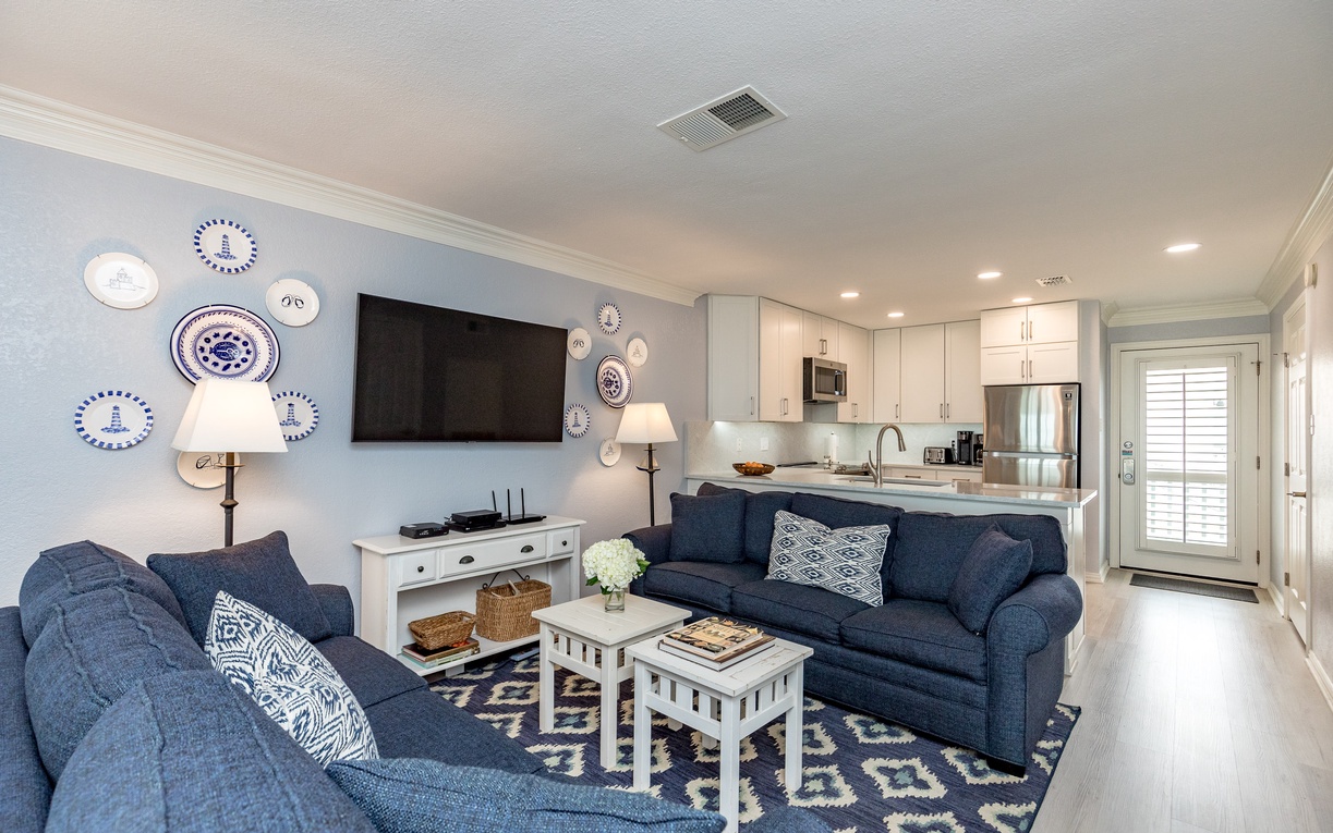Relax in your beautifully appointed living space featuring comfortable navy seating, charming coastal décor, and a fully equipped kitchen perfect for home-cooked meals.