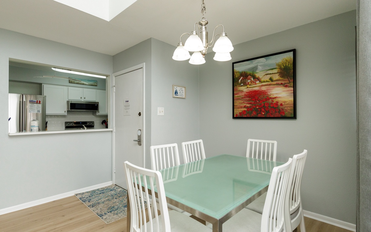 Your bright dining space features a glass-top table for six, perfect for family meals under the elegant chandelier.