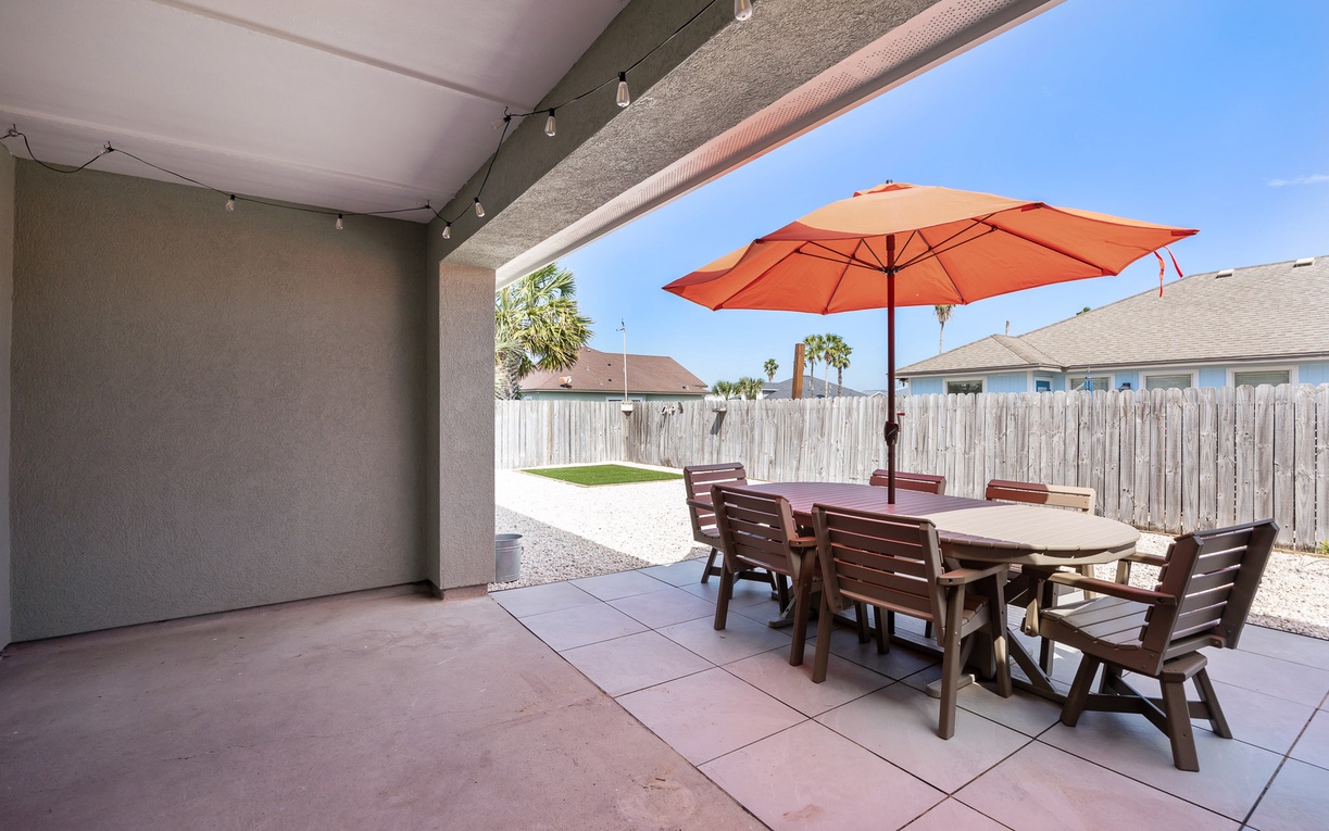 Your covered patio offers perfect shade for outdoor dining, with a spacious table and cheerful umbrella overlooking your private fenced yard.