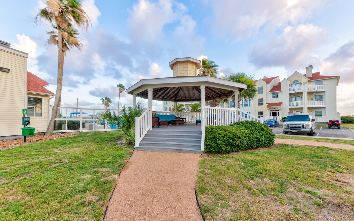 A charming beachside pavilion nestled among palm trees and coastal homes, offering a peaceful gathering spot in this tropical neighborhood.