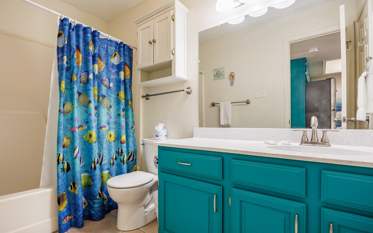 Refresh in your vibrant turquoise bathroom featuring tropical fish-themed shower curtain and spacious vanity with ample storage.