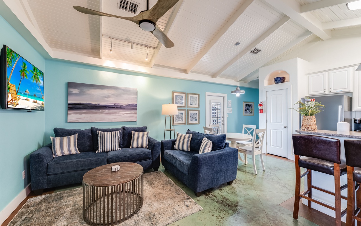 Unwind in this bright, coastal-inspired living space with soaring ceilings, plush navy seating, and tropical artwork that instantly puts you in vacation mode.