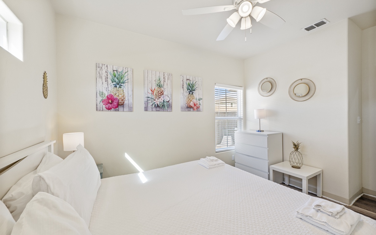 Unwind in your bright, tropical-themed bedroom with cheerful pineapple art, plush linens, and gentle ceiling fan breezes creating your perfect retreat.