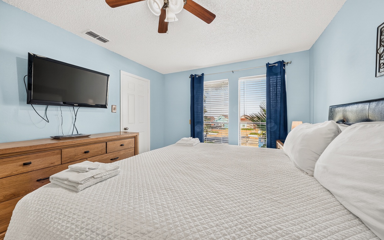 Unwind in your tranquil bedroom with soft blue walls, a plush bed dressed in crisp linens, and a gentle breeze from the ceiling fan overhead. Fresh towels await your arrival.