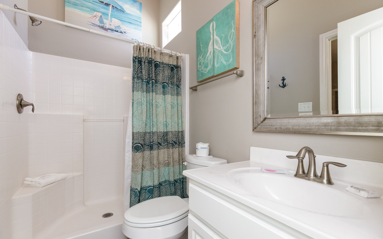 Fresh coastal-themed bathroom featuring white fixtures, walk-in shower, and charming nautical artwork to enhance your beachside retreat experience.