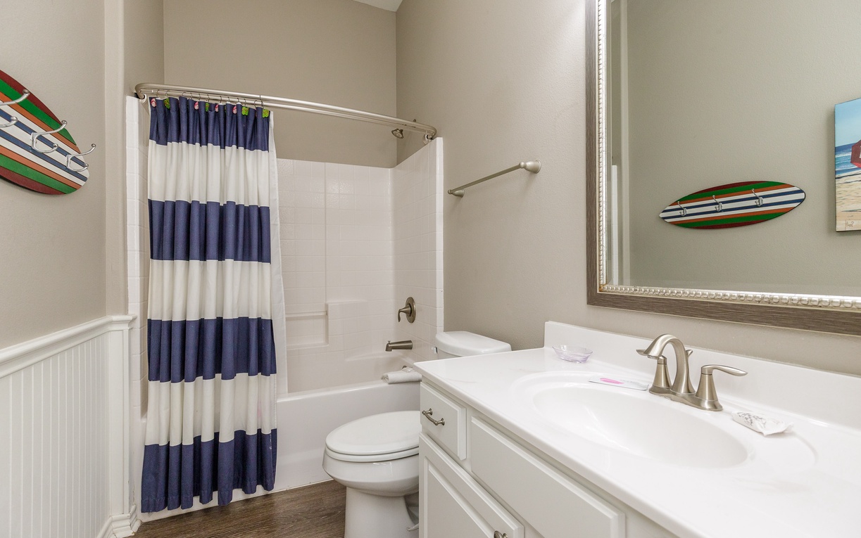 Refresh in your nautical-themed bathroom with striped curtains, white vanity, and colorful surfboard decor creating coastal charm.