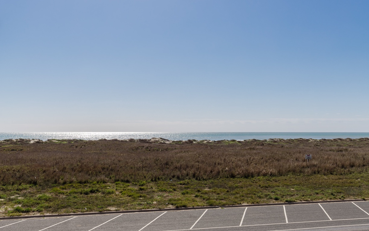Coastal parking area with natural vegetation leading to ocean views under clear blue skies.