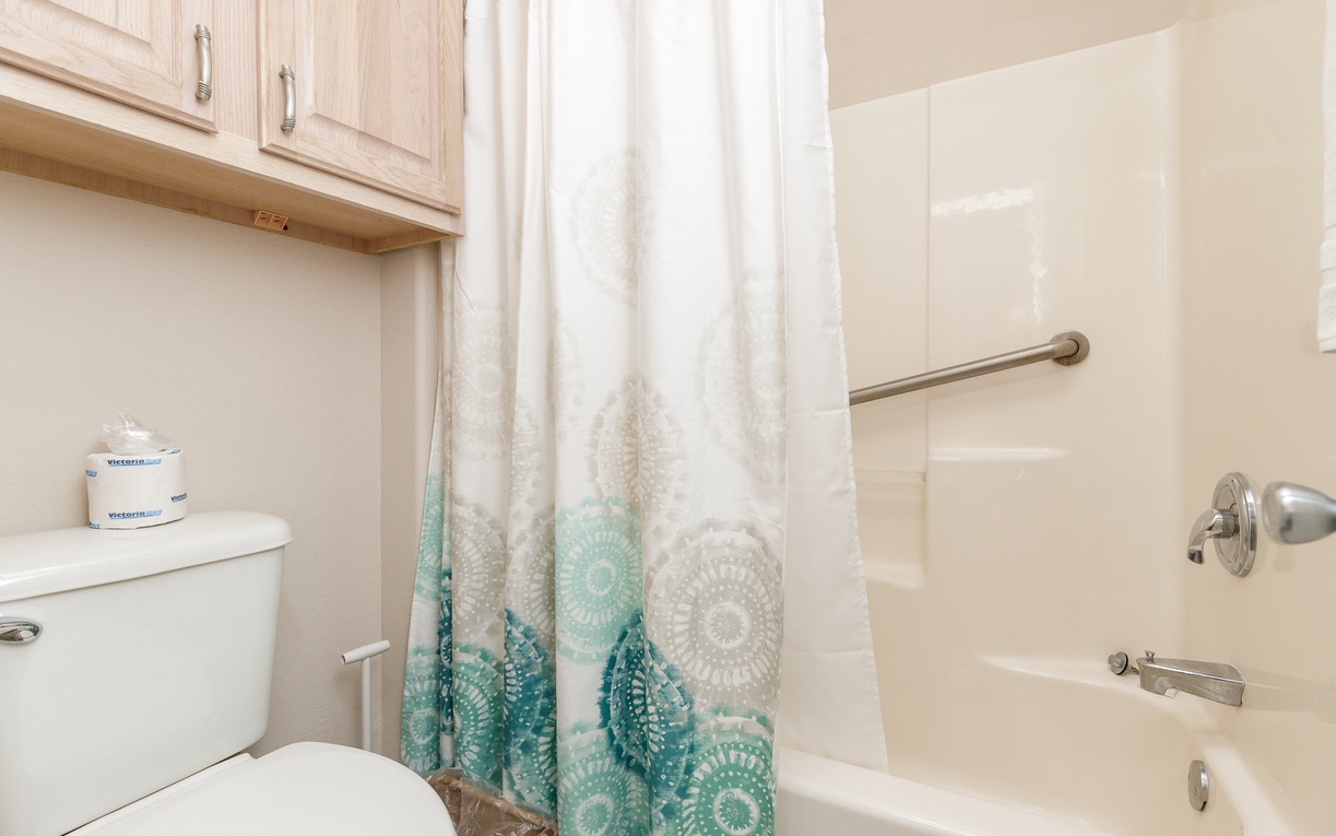 Your private bathroom features a relaxing tub-shower combo with cheerful teal accents and convenient storage above the toilet.