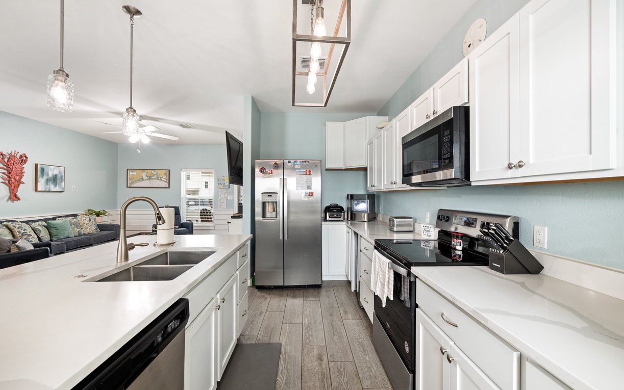 Your fully equipped kitchen invites you to prepare delicious meals with modern appliances, ample counter space, and crisp white cabinetry, while soft blue walls and bright lighting create a fresh, welcoming atmosphere.