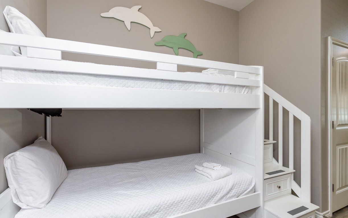 Rest comfortably in this charming bunk bed setup, complete with fresh linens and playful dolphin wall art for a cozy coastal vibe.