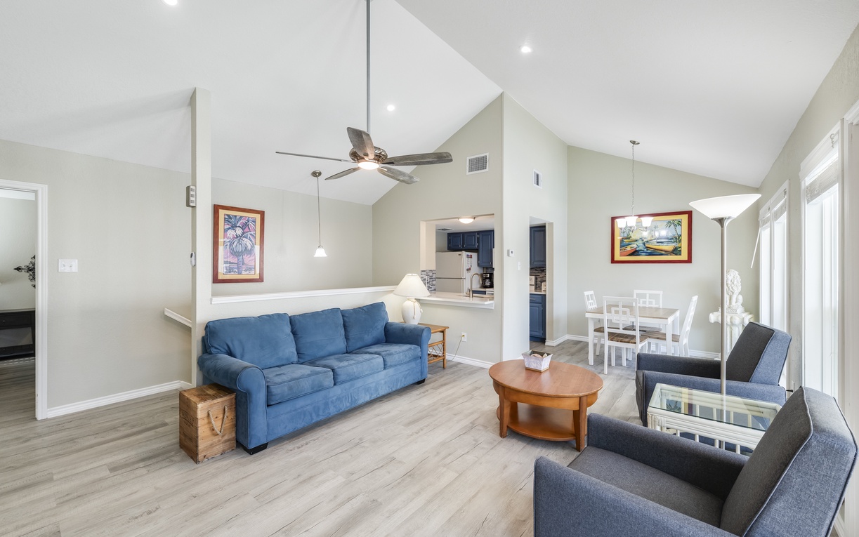 Relax in your spacious open-plan living area with vaulted ceilings, sleeper sofa, and coastal artwork creating a serene atmosphere.