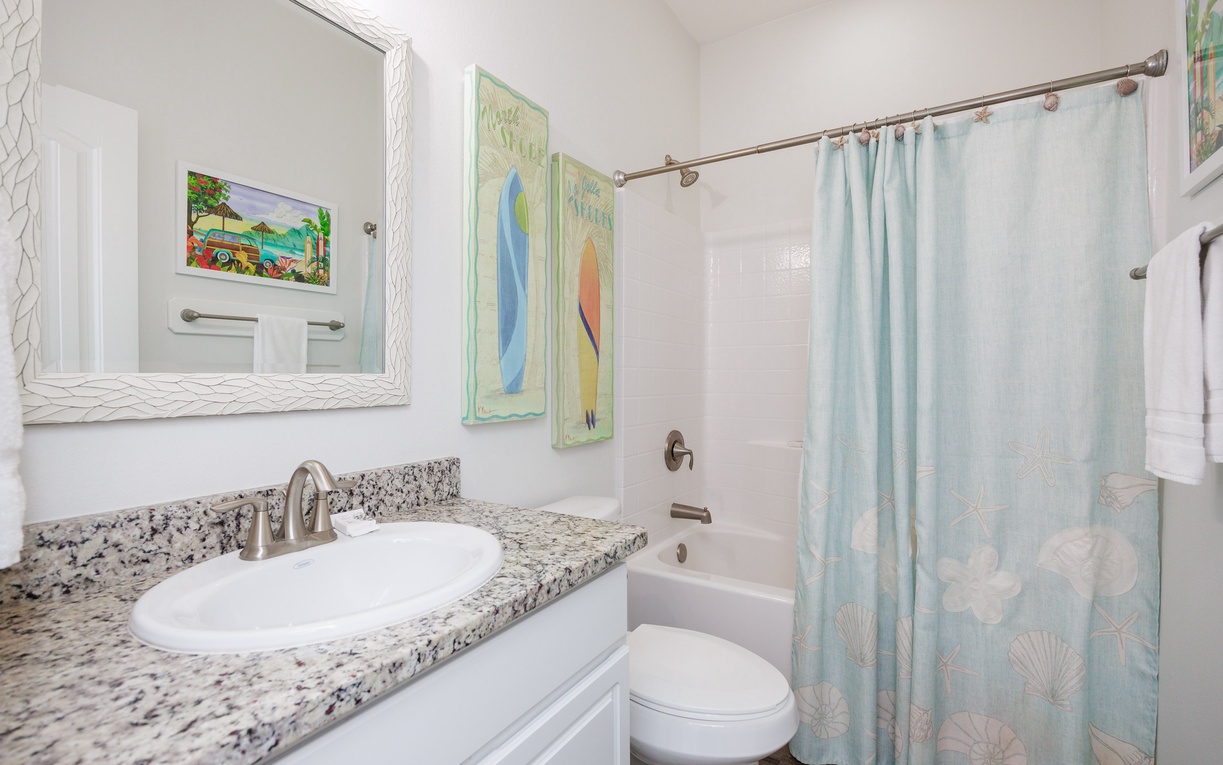 Refresh in your pristine bathroom featuring granite countertops, coastal artwork, and a relaxing tub-shower combo with cheerful beach-themed curtain.