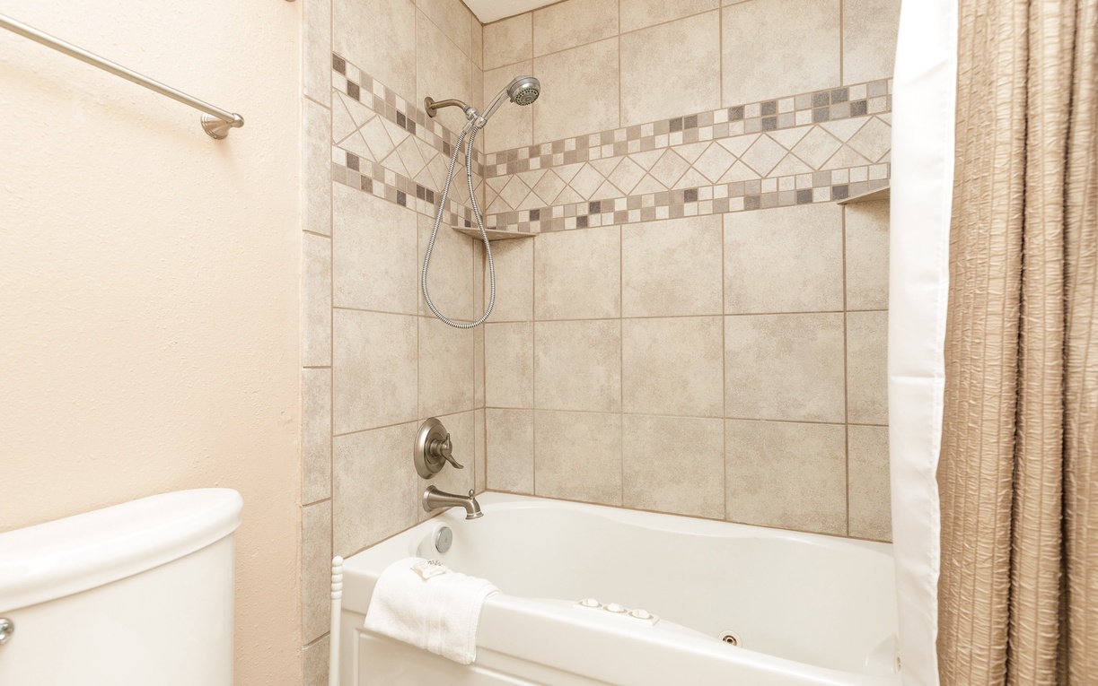 Relax in your elegant tiled bathroom featuring a deep soaking tub with shower combo and warm neutral tones.