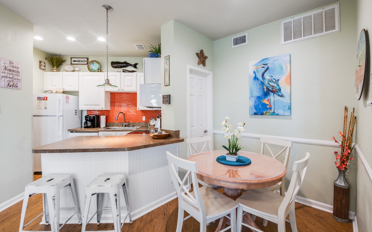 Gather around your bright coastal kitchen featuring warm wood counters, beach-themed decor, and a cozy dining nook perfect for morning coffee.