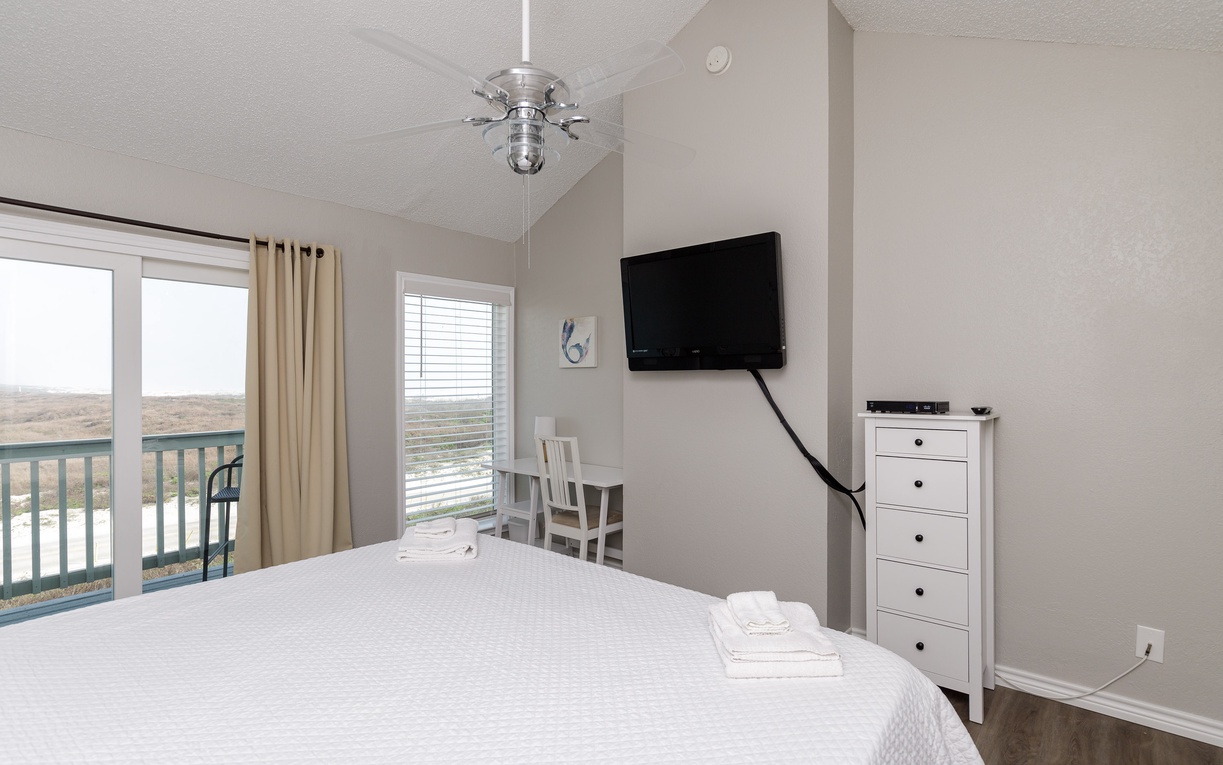 Relax in your serene bedroom with balcony access, flat-screen TV, and comfy seating nook overlooking peaceful natural views.