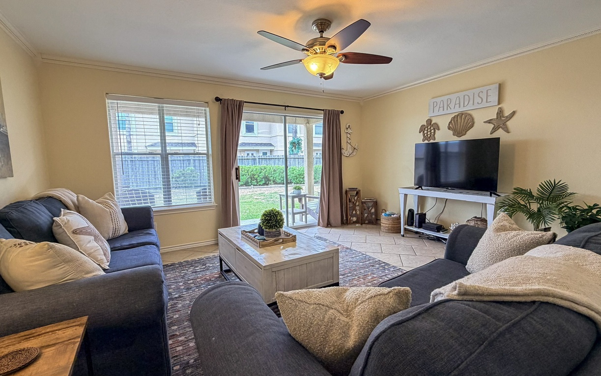 Unwind in your spacious living room with plush seating, entertainment center, and calming coastal decor that sets the perfect vacation mood.