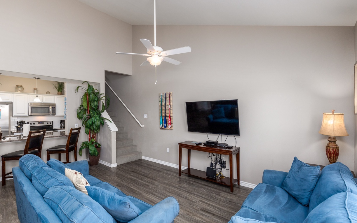 Relax in your open-concept living space with comfortable blue sofas, modern TV entertainment, and kitchen views.