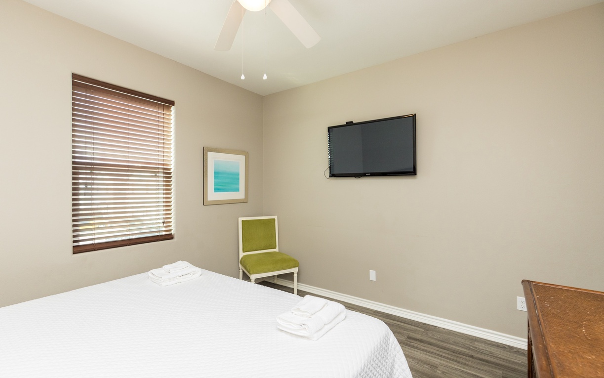 Unwind in your serene bedroom with crisp linens, ceiling fan, and wall-mounted TV for cozy nights in.