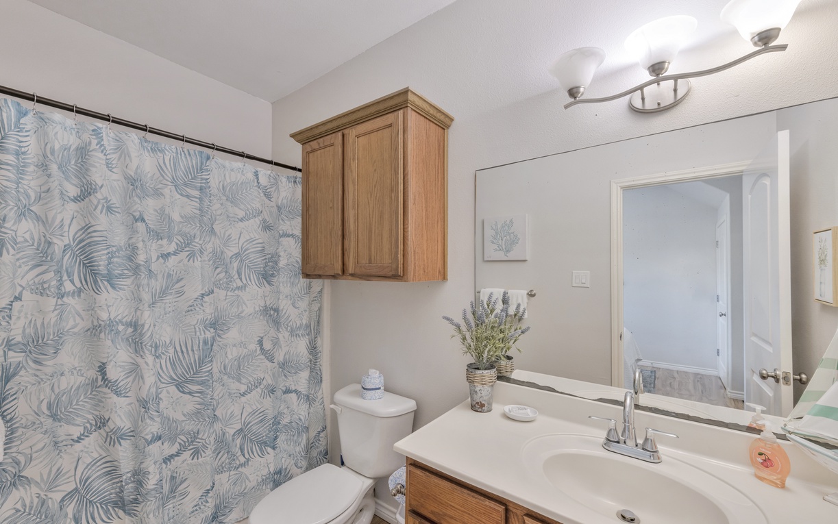 Refresh in your beautifully appointed bathroom with tropical-inspired shower curtains, warm wood cabinets, and thoughtful touches like fresh lavender.
