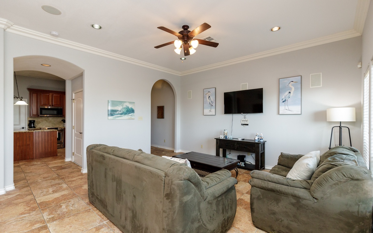 Relax in your spacious living room featuring plush seating, ocean-inspired artwork, and an open layout connecting to the kitchen.