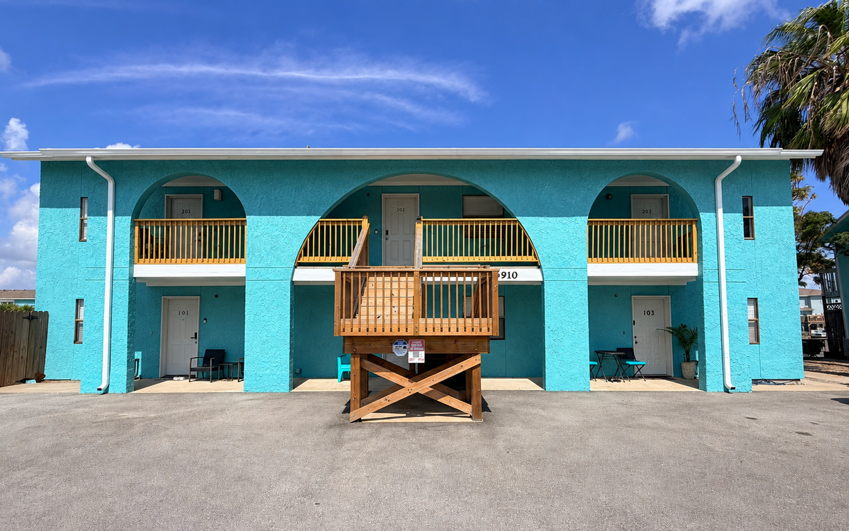 Mediterranean-style building features distinctive arched balconies and vibrant turquoise doors under endless blue skies.