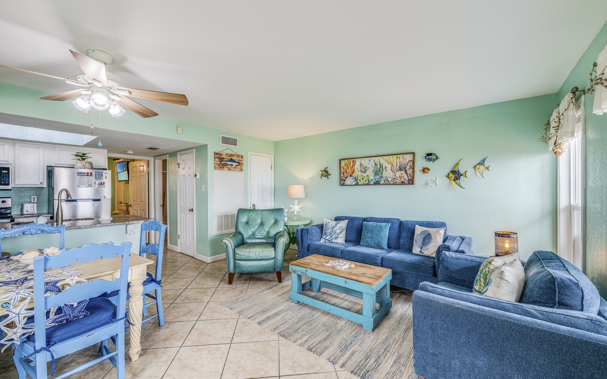 Relax in your coastal-themed living room with ocean-inspired decor, comfortable blue seating, and an open kitchen for easy entertaining.