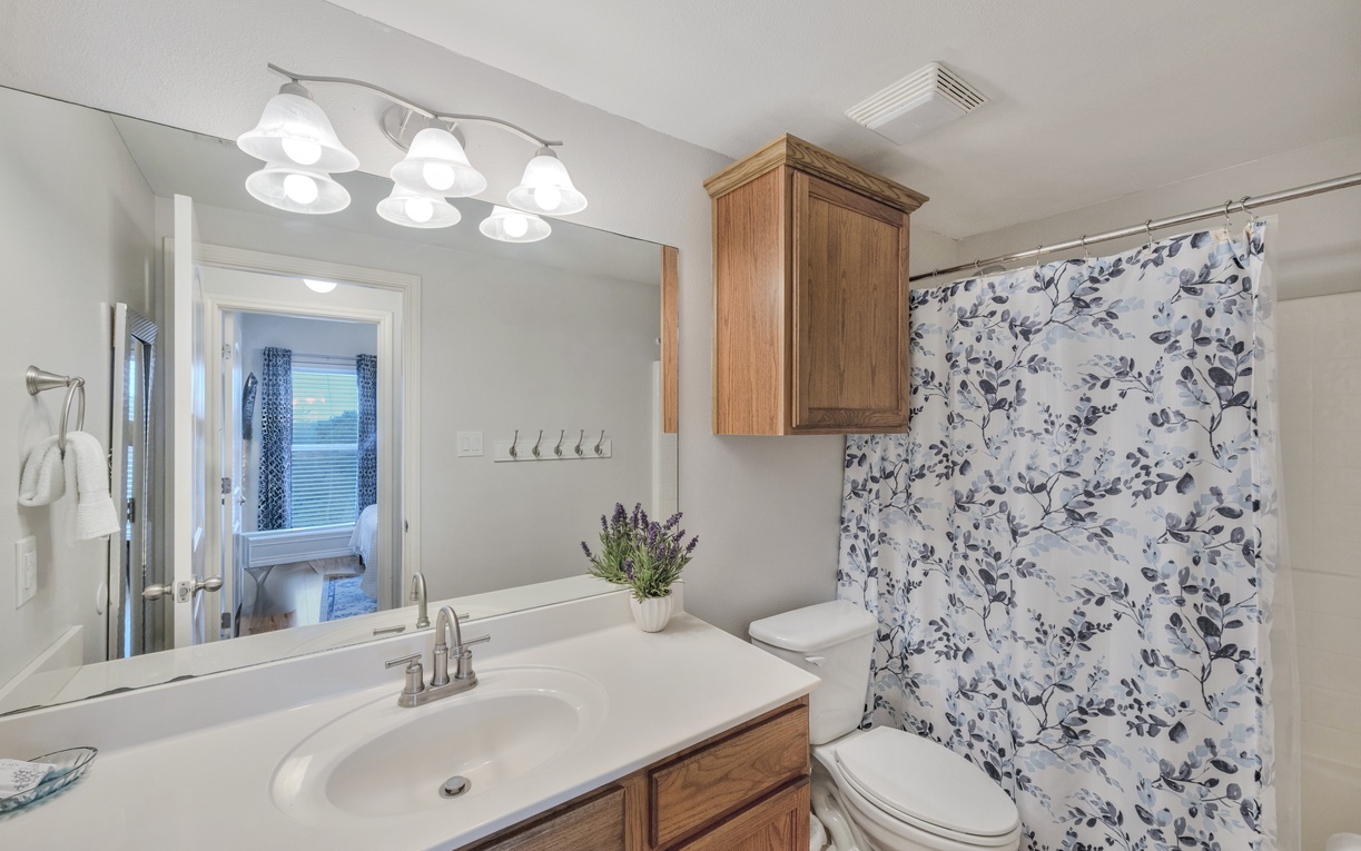 Refresh in your private bathroom featuring a soaking tub with charming floral curtain, warm wood vanity, and plenty of space to unwind.