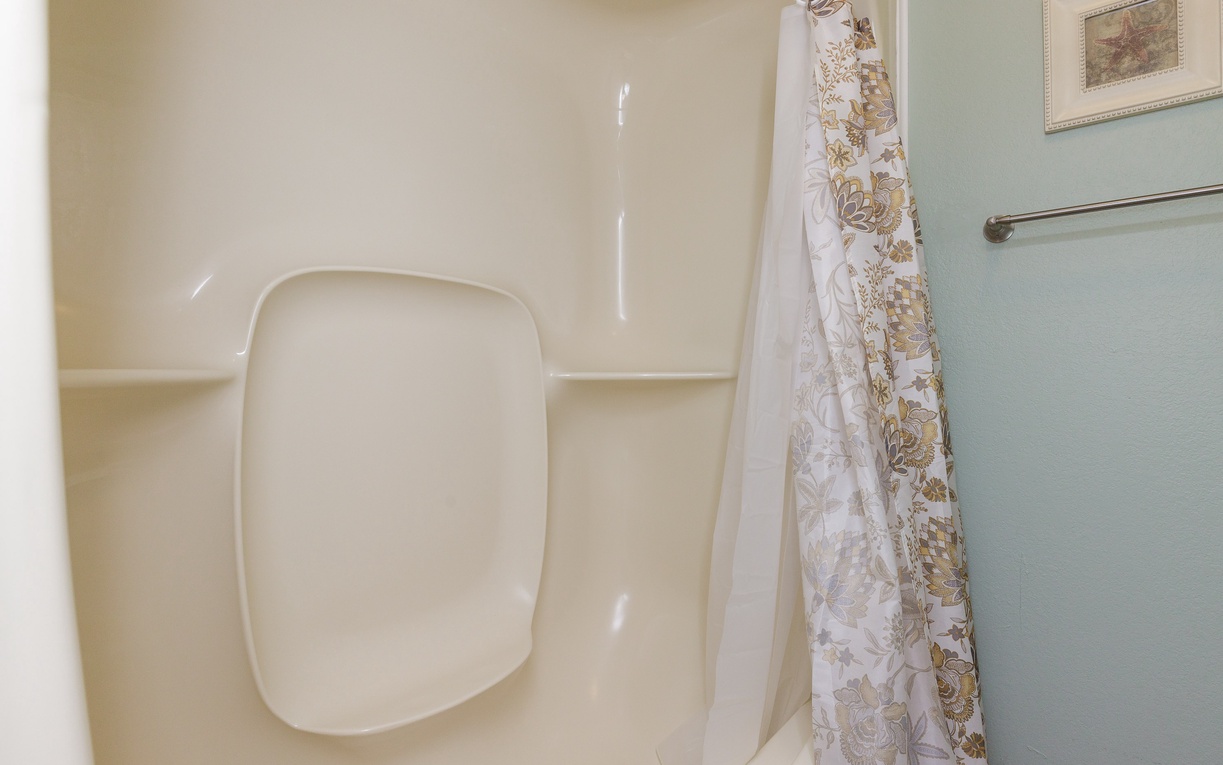 Step into your private bathroom where a clean, spacious shower awaits with decorative curtain and convenient built-in seating.