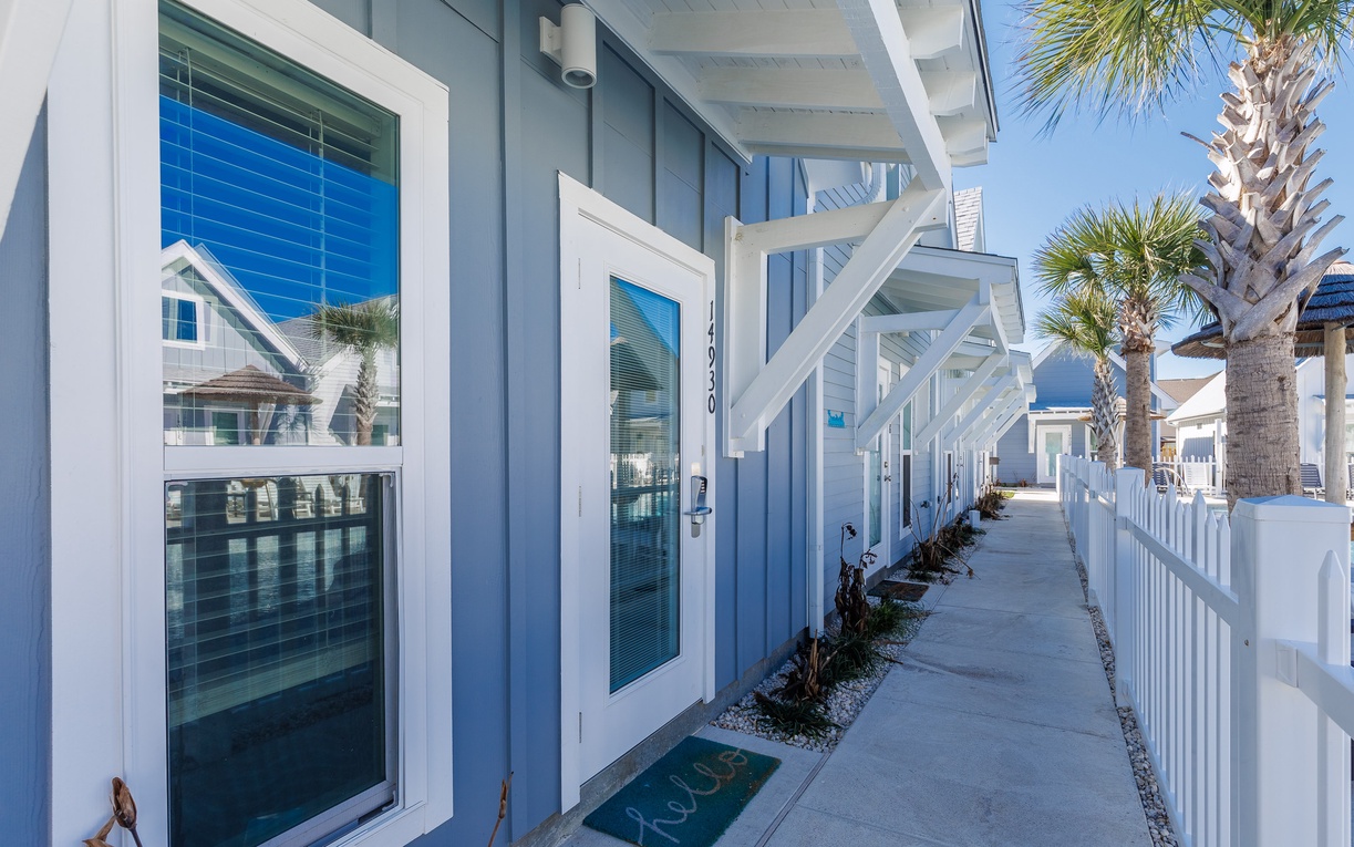 Modern coastal property entrance with blue siding, white trim, and tropical palms welcoming guests to their beachside getaway.