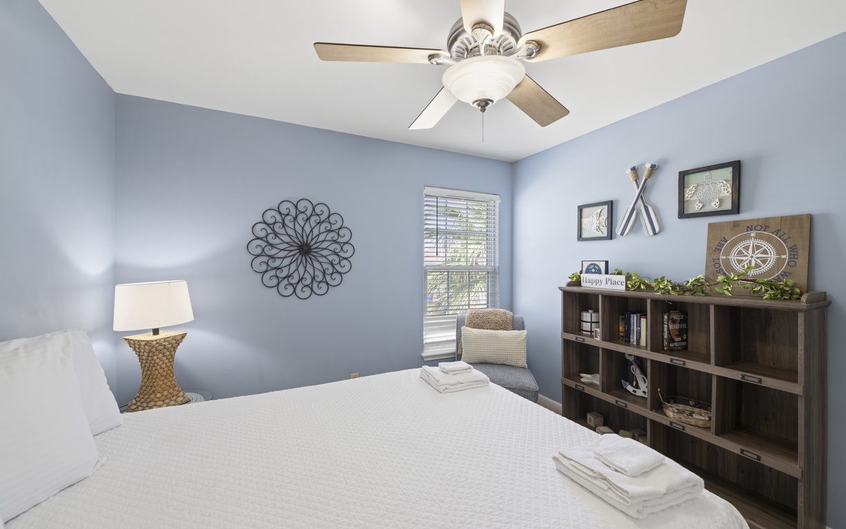 Sink into restful sleep in this serene bedroom with calming blue walls and a plush bed, where thoughtful decor and a gentle ceiling fan breeze help you unwind after your daily adventures.