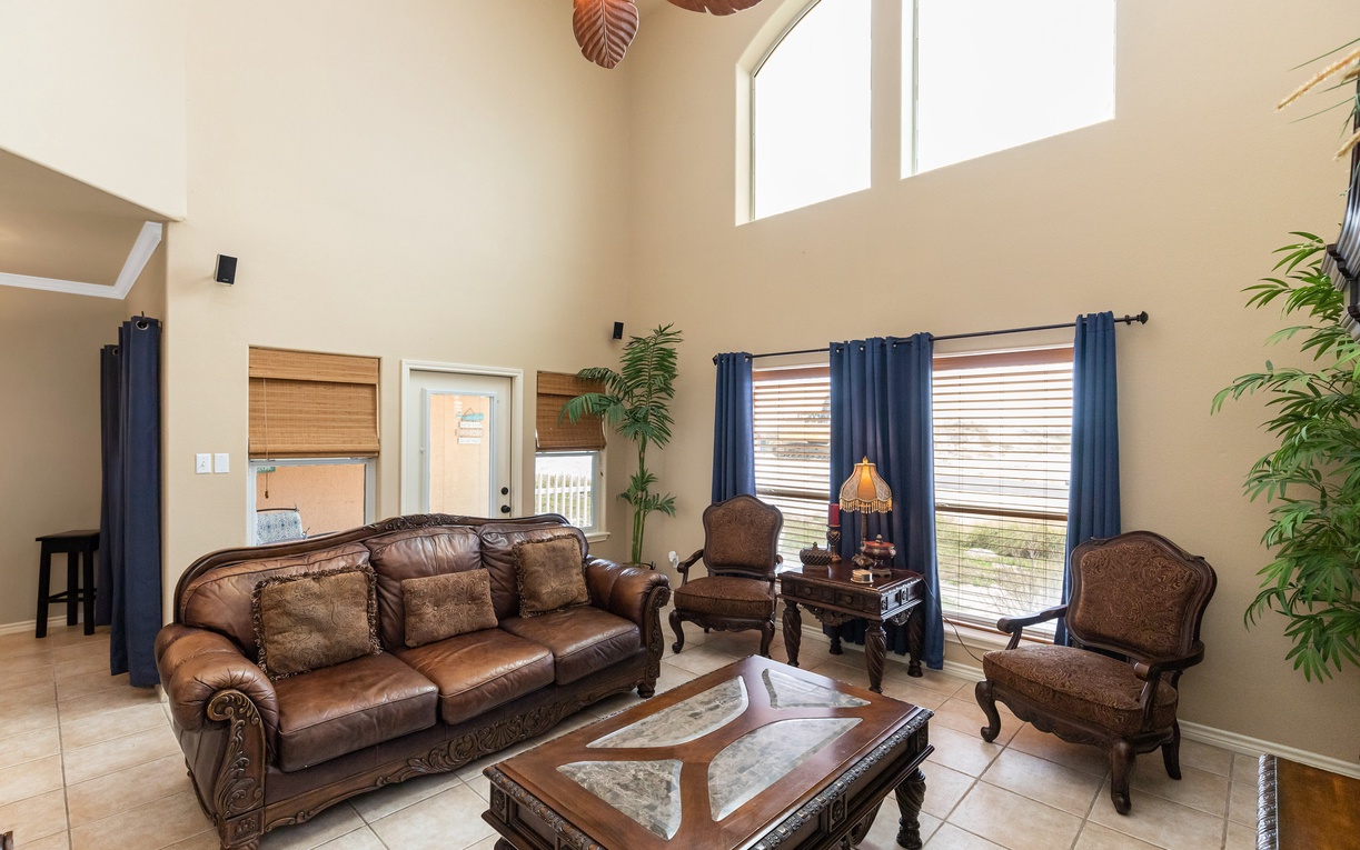 Relax in your elegant living room with rich leather seating, tropical ceiling fan, and abundant natural light streaming through tall windows.