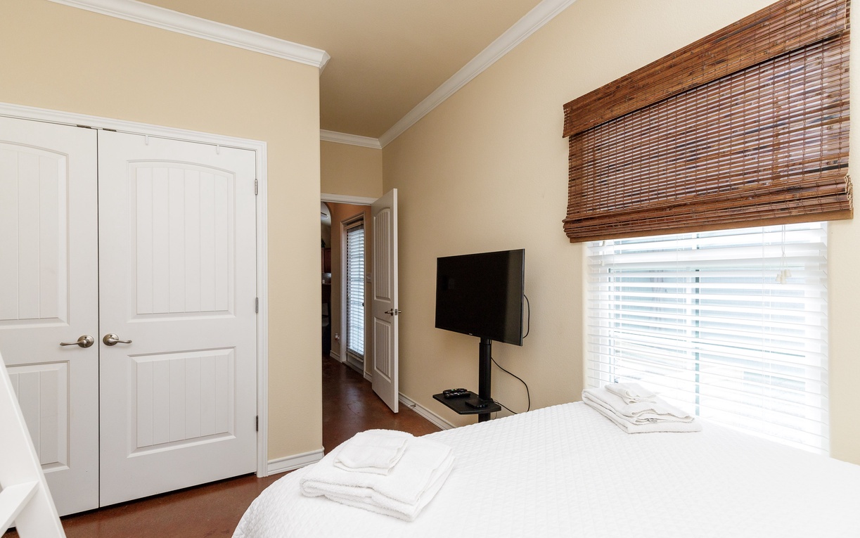 Your peaceful bedroom features a comfortable bed, flat-screen TV, and warm bamboo blinds that filter natural light beautifully.