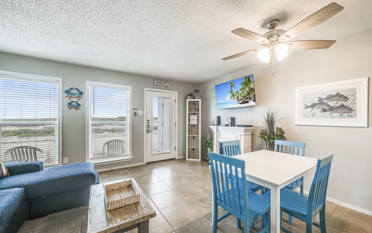 Your bright, coastal-themed living space features cheerful blue dining chairs and ocean views from large windows—perfect for morning coffee.