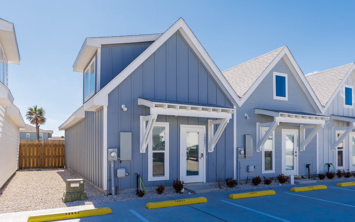 Modern blue cottage-style building with white trim and covered entrance porches in a sunny coastal setting.
