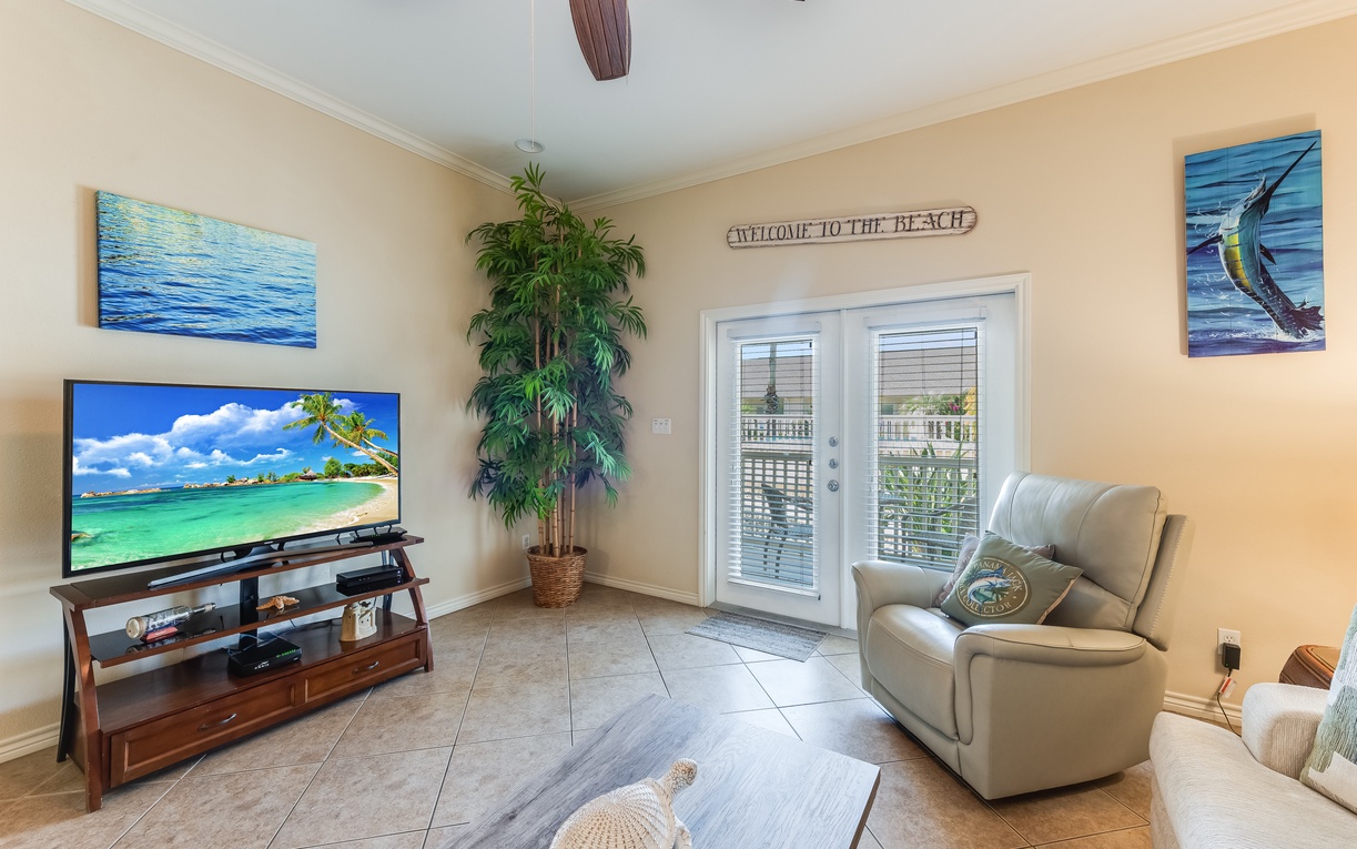 Sink into comfortable seating while watching your favorite shows on the large TV in this beach-themed living space with tropical artwork.