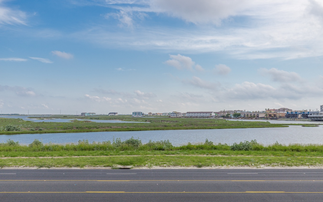Scenic waterfront community with marshlands and residential homes stretching along the peaceful shoreline under expansive coastal skies.