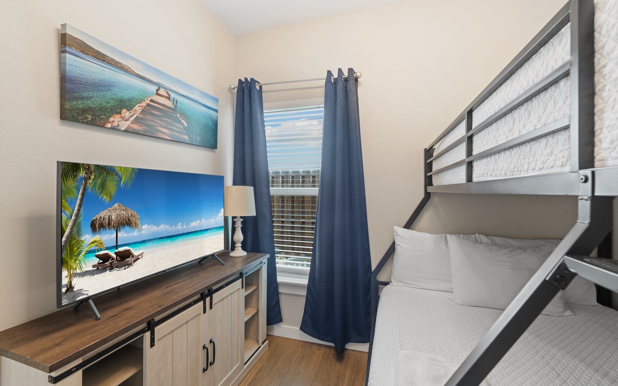 Your coastal-inspired bedroom features a comfy bunk bed and large TV for family movie nights, with soft lighting and cheerful beach artwork creating a relaxing, vacation-ready atmosphere.